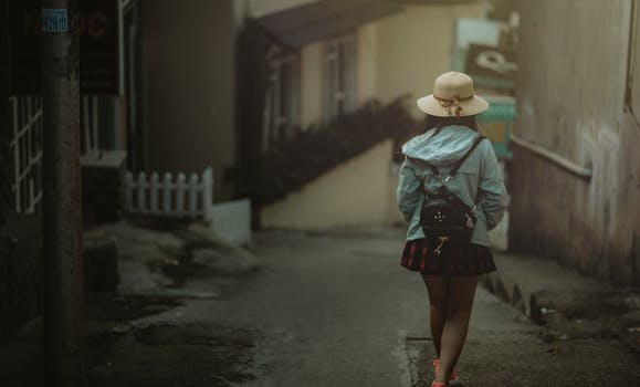 白天，一位背着背包的年轻女子漫步在一条安静的城市小巷里