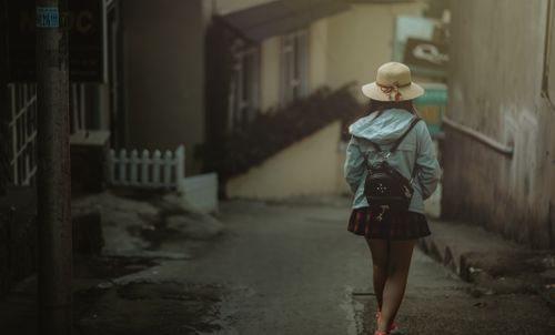 Free A young woman with a backpack strolls through a quiet urban alleyway in daylight. Stock Photo