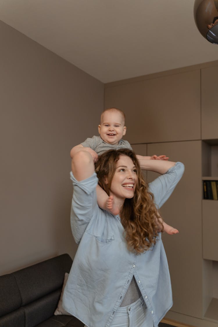 A Woman Carrying Her Baby Boy On Her Shoulders