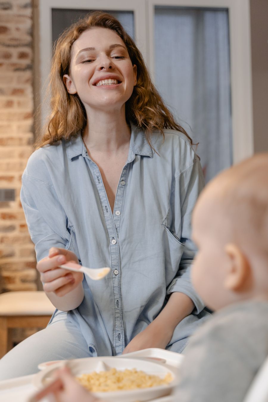 mother gently feeding her baby with a spoon at the family dinner table