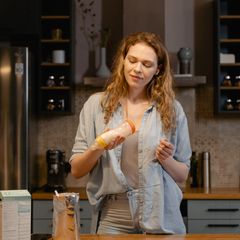 Young mother in a denim shirt shaking a freshly made baby bottle in a warm modern kitchen