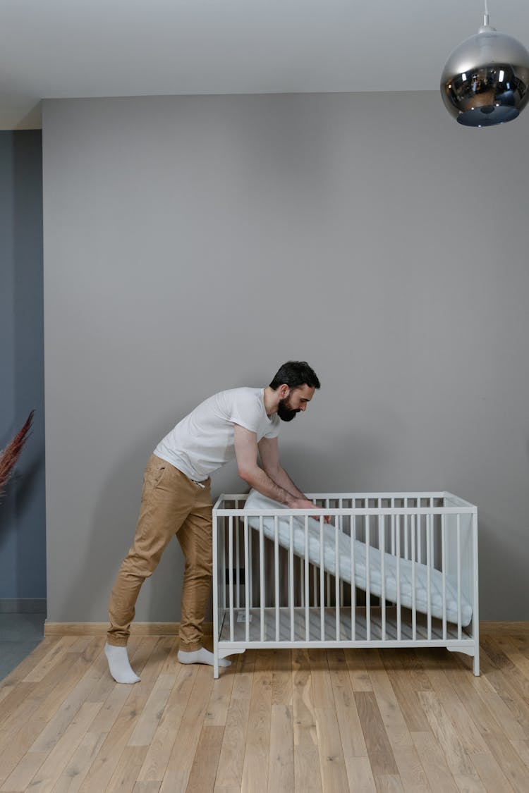 A Man Putting A Mattress In A Crib