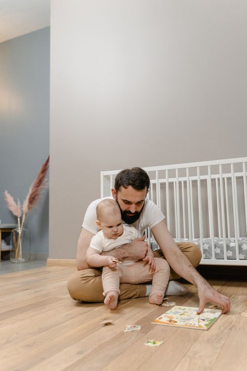 Free Father and baby sitting on the floor, playing with a puzzle together, capturing a joyful moment of bonding at home. Stock Photo