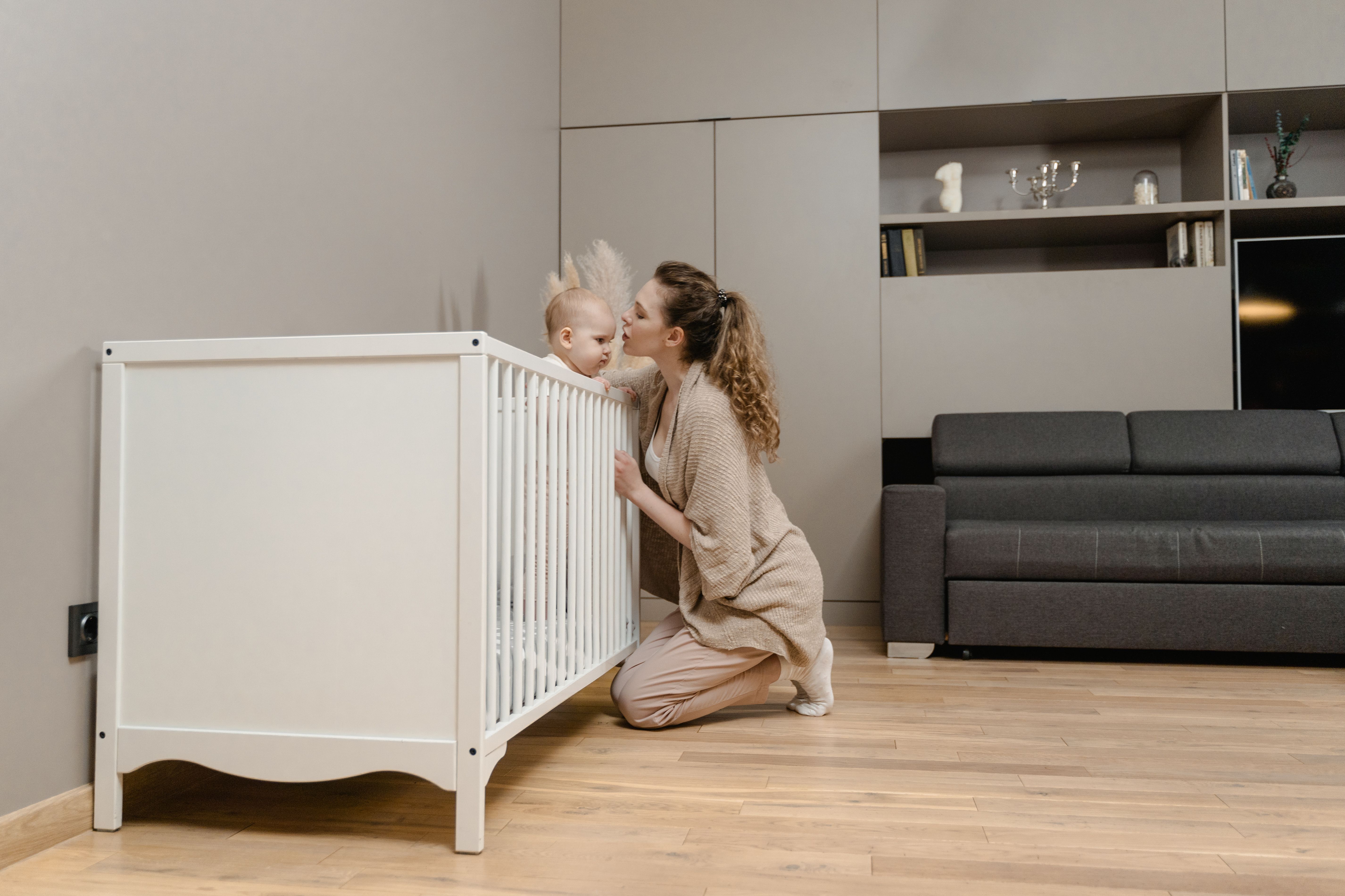 A mother lovingly kisses her baby inside a minimalistic modern nursery with stylish decor.