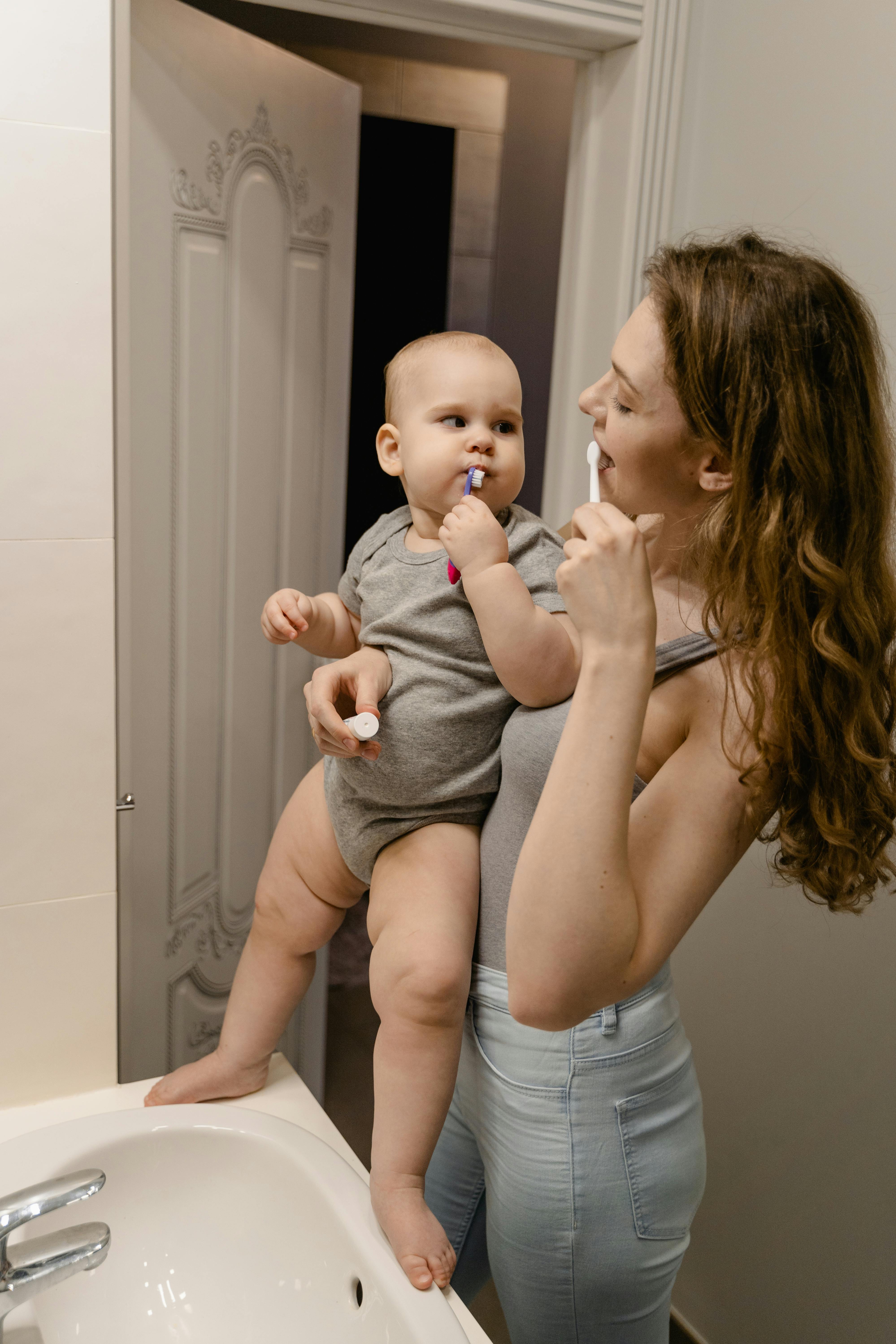 Mother and baby bonding while brushing teeth together in a bathroom.