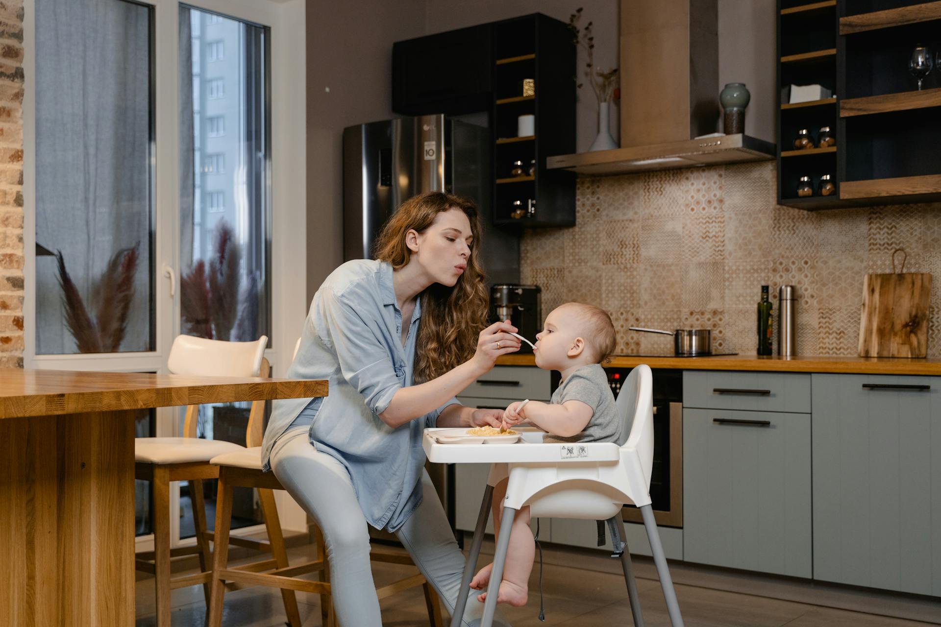 A Woman Feeding Her Baby Sitting on the High Chair