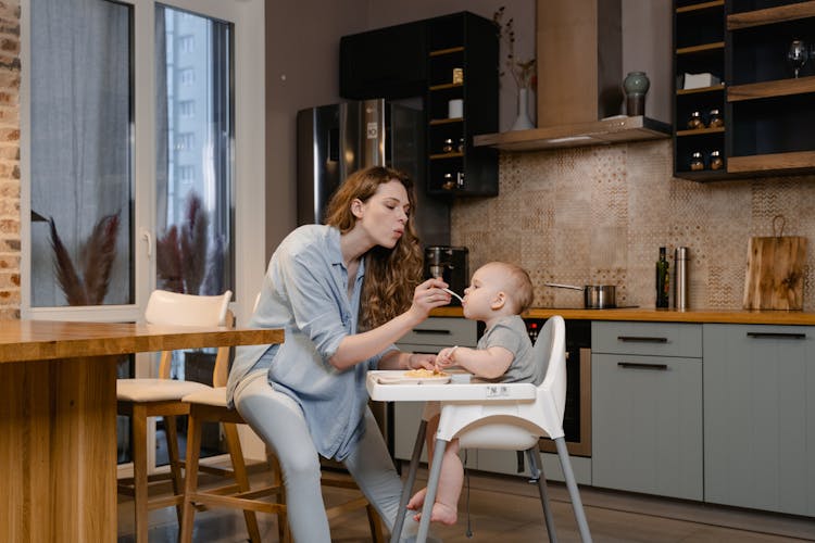 A Woman Feeding Her Baby Sitting On The High Chair