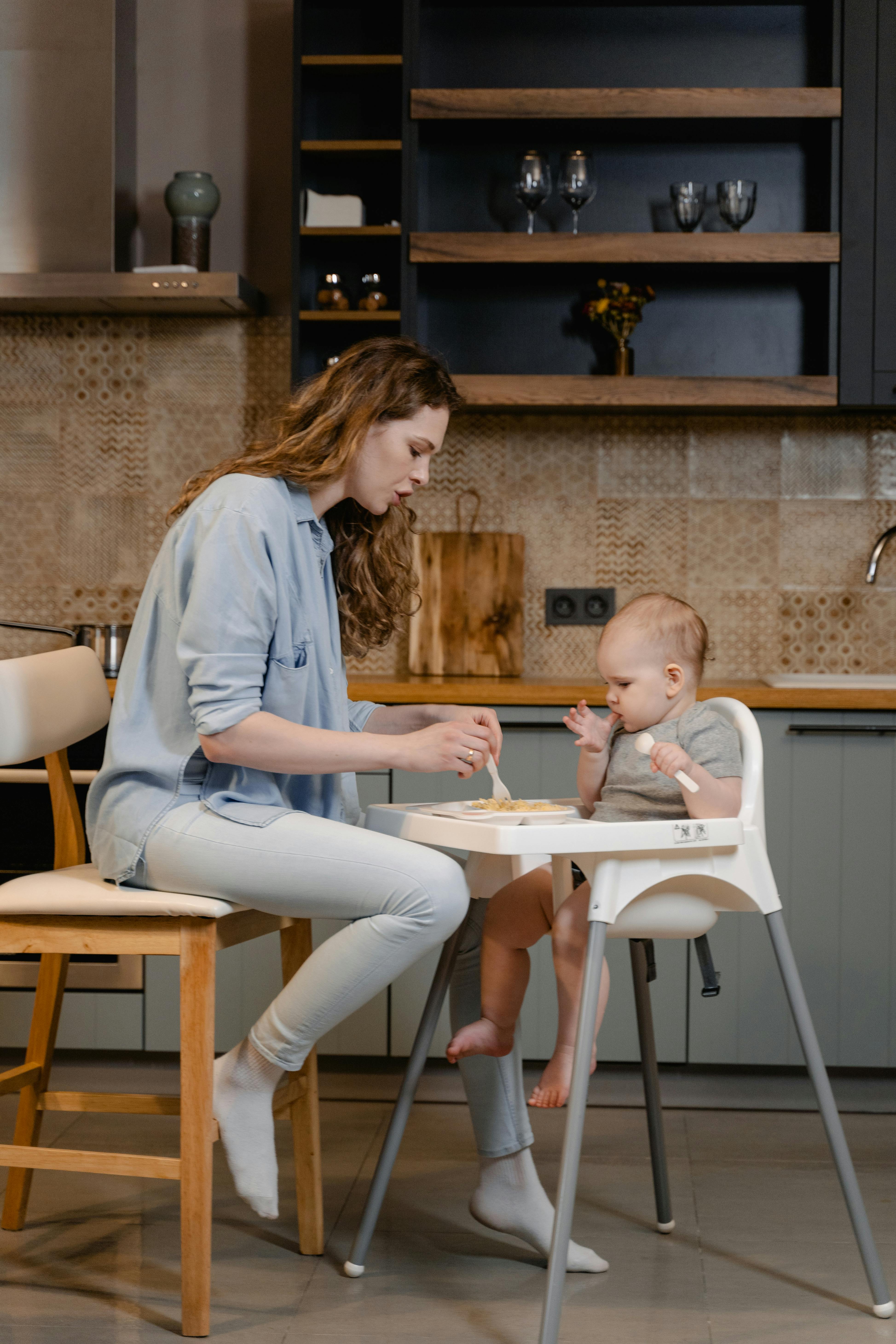 a woman sitting on the chair while feeding her baby