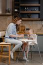 A Woman Sitting on the Chair while Feeding Her Baby
