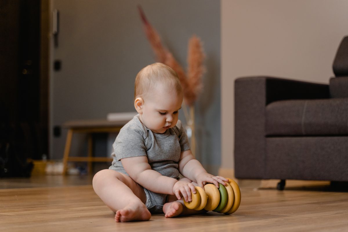 Baby sitting on the floor and exploring a wooden stacking toy.