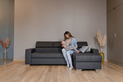 Free A Woman Sitting on the Couch while Breastfeeding Her Baby Stock Photo