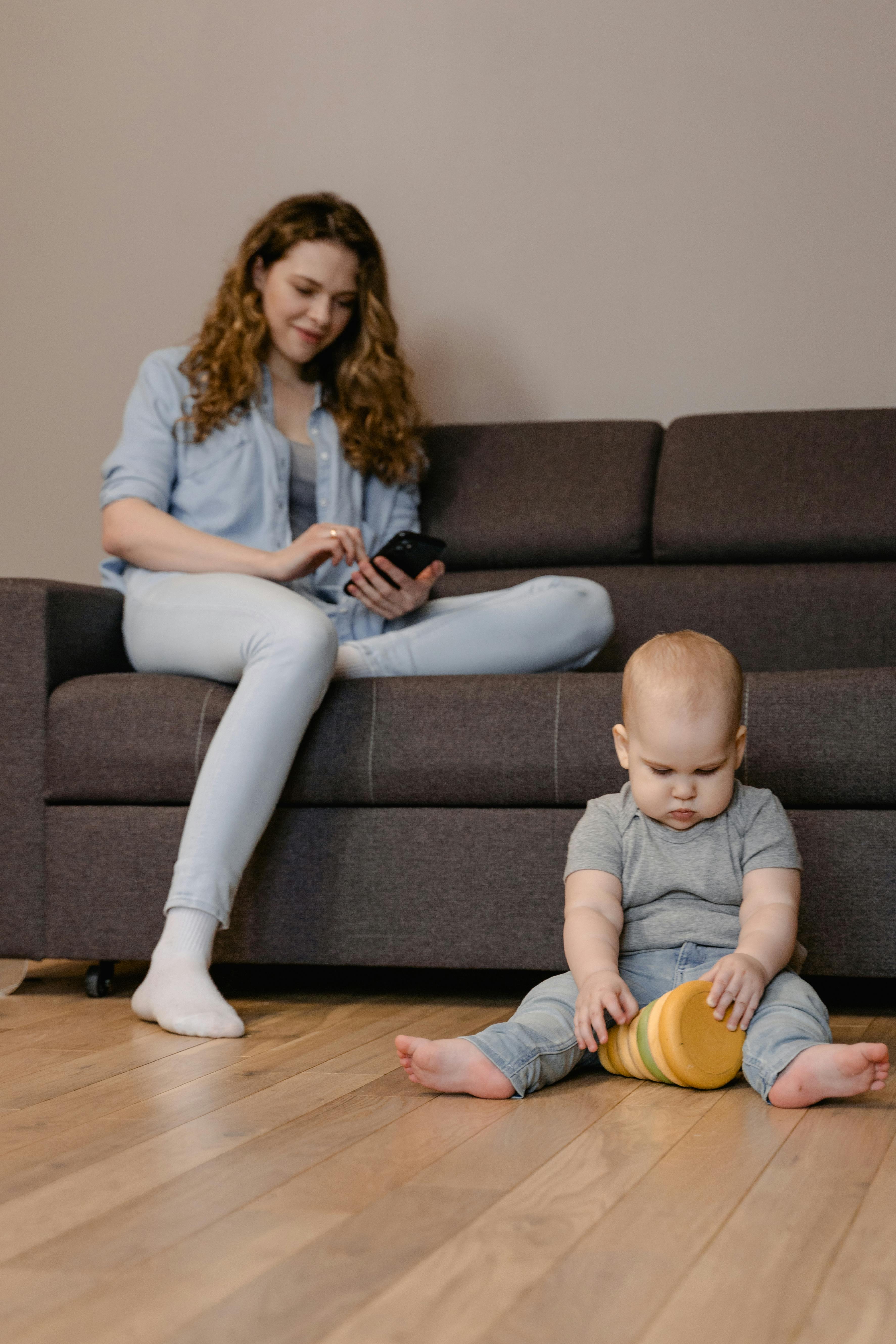 a woman using her mobile phone near her baby sitting on the floor