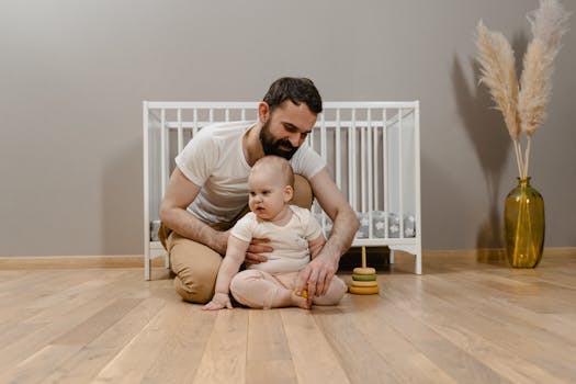 Dad and baby sharing a playful moment on the wooden floor next to a crib.