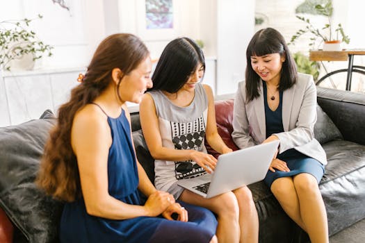 Three businesswomen collaborating in a modern office setting using a laptop, promoting teamwork.
