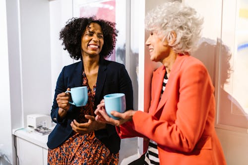 Two diverse women enjoying coffee together in a modern office setting.