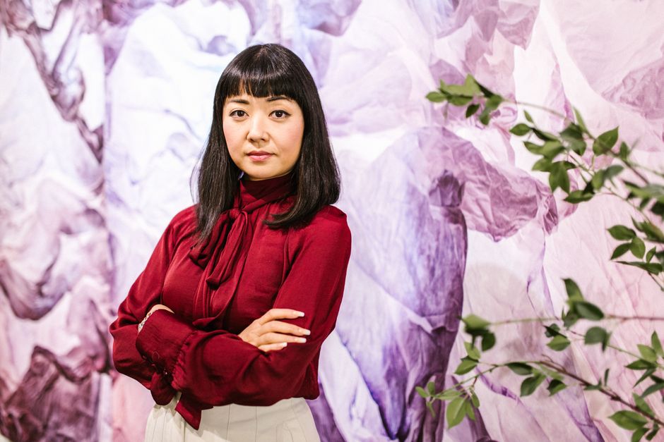 赤い服を着たビジネスウーマンが、自信を持ってアートなオフィスの背景の前で腕を組んでいます。