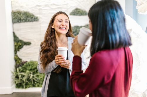 Free Two women in a modern office setting enjoying a casual coffee break, highlighting teamwork and relaxation. Stock Photo