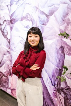 Smiling businesswoman in red blouse and white pants in a creative office setting.