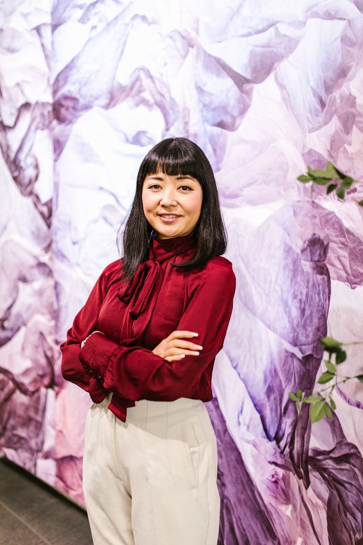 A Woman In Red Long Sleeves And White Pants Smiling With Her Arms Crossed