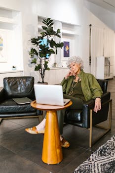 Senior woman in stylish attire working remotely in a modern office, seated with a laptop.