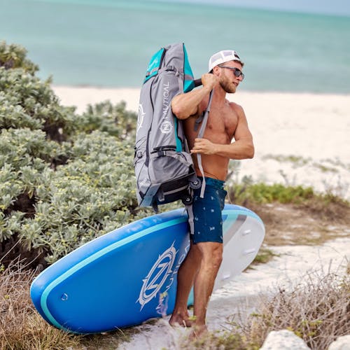 Man in Blue Shorts standing beside a Blue Surfboard