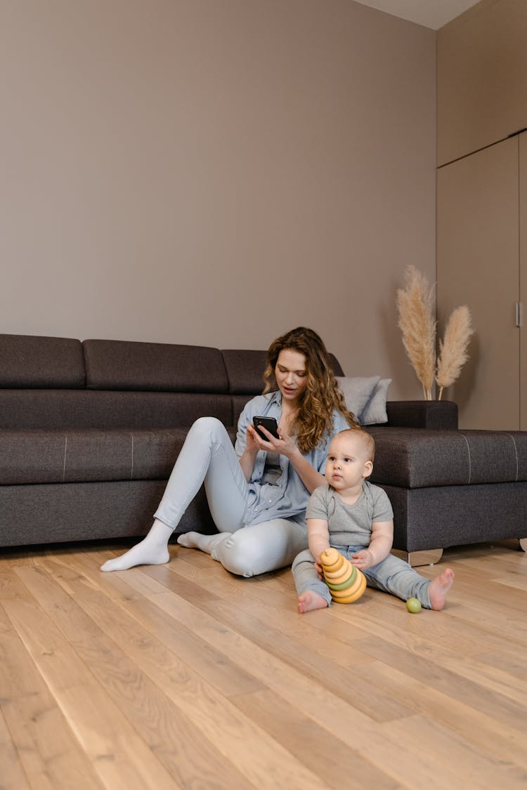 Photo Of A Mother Using Her Phone Beside Her Child