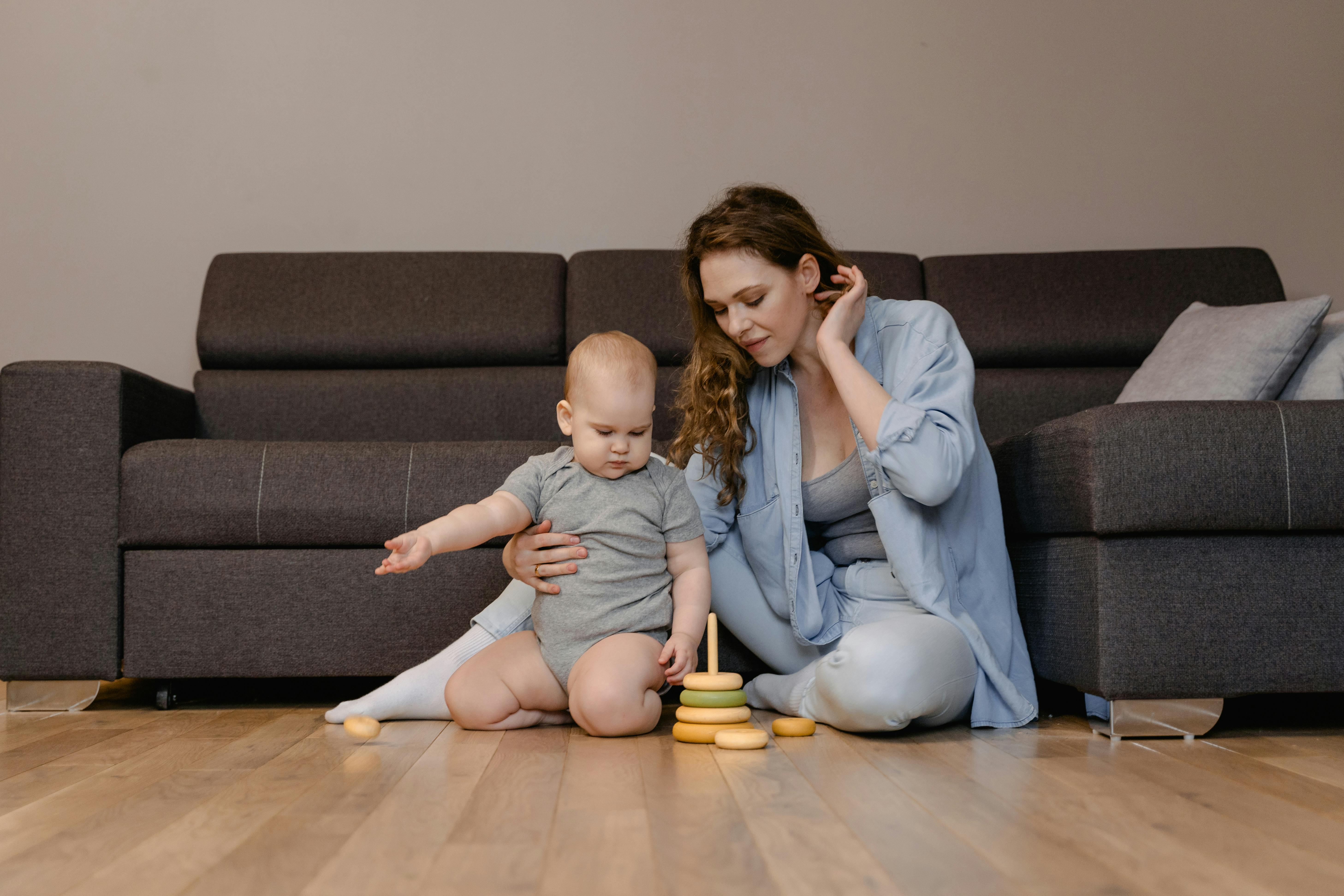 a woman sitting on floor with a baby looking at a stacking ring toy