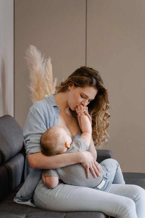 坐在長沙發上抱著嬰兒的灰色長袖襯衫的女人