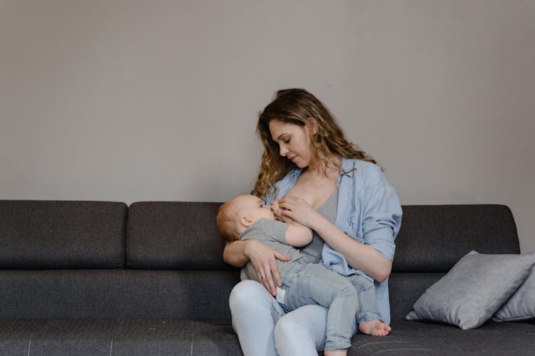 A Woman Breastfeeding Her Baby While Sitting On The Couch