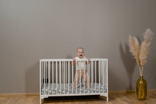 A Cute Baby Smiling while Standing Inside the Crib