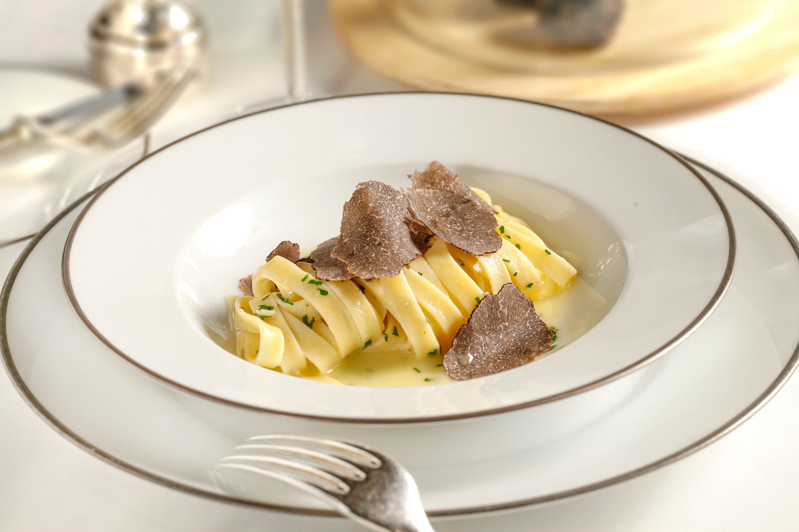 Pasta fresca all'uovo con lamelle di tartufo nero su piatto bianco filettato