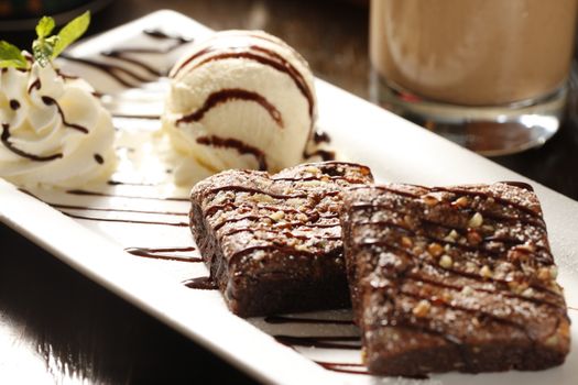 Decadent brownies with vanilla ice cream and whipped cream on a white plate.