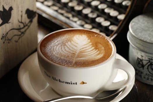 Close-up of a latte with leaf art in a branded cup on a saucer, surrounded by vintage decor.
