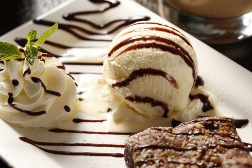 Free Delicious brownie served with vanilla ice cream and whipped cream, drizzled with chocolate syrup, on a ceramic plate. Stock Photo