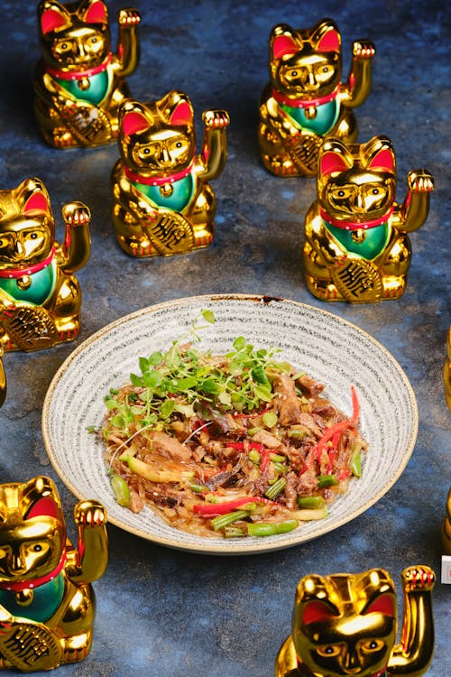 Free Salad on Ceramic Plate Beside Lucky Cat Traditional Ceramic Figurines Stock Photo