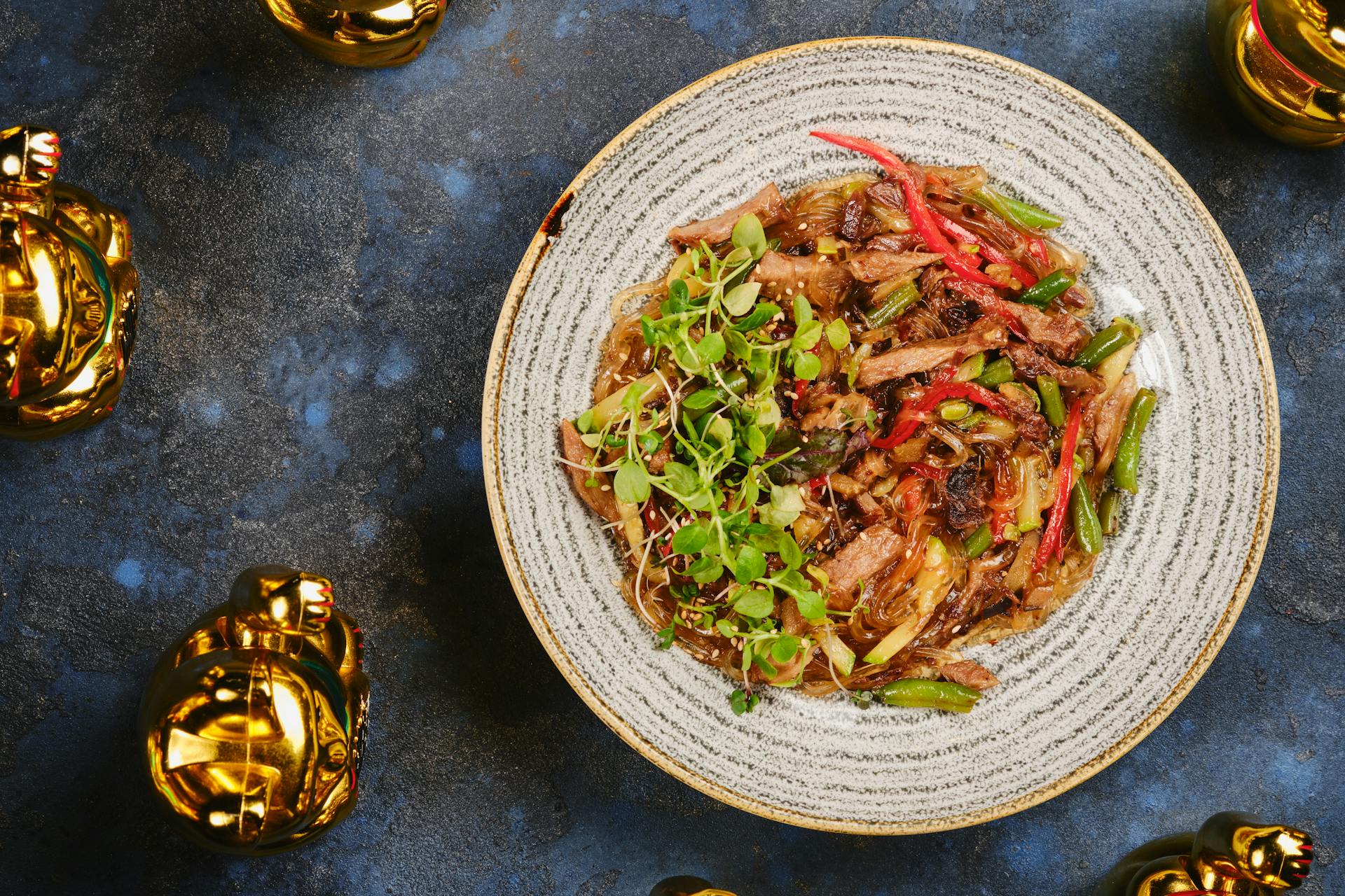 Colorful Vietnamese noodle dish with golden lucky cats on a textured surface.