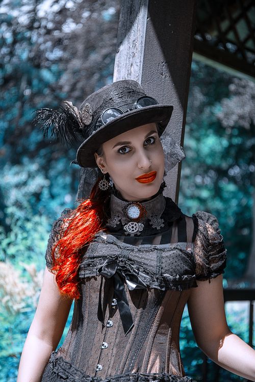 Free Woman in steampunk attire with red hair poses outdoors in a park under sunlight. Stock Photo