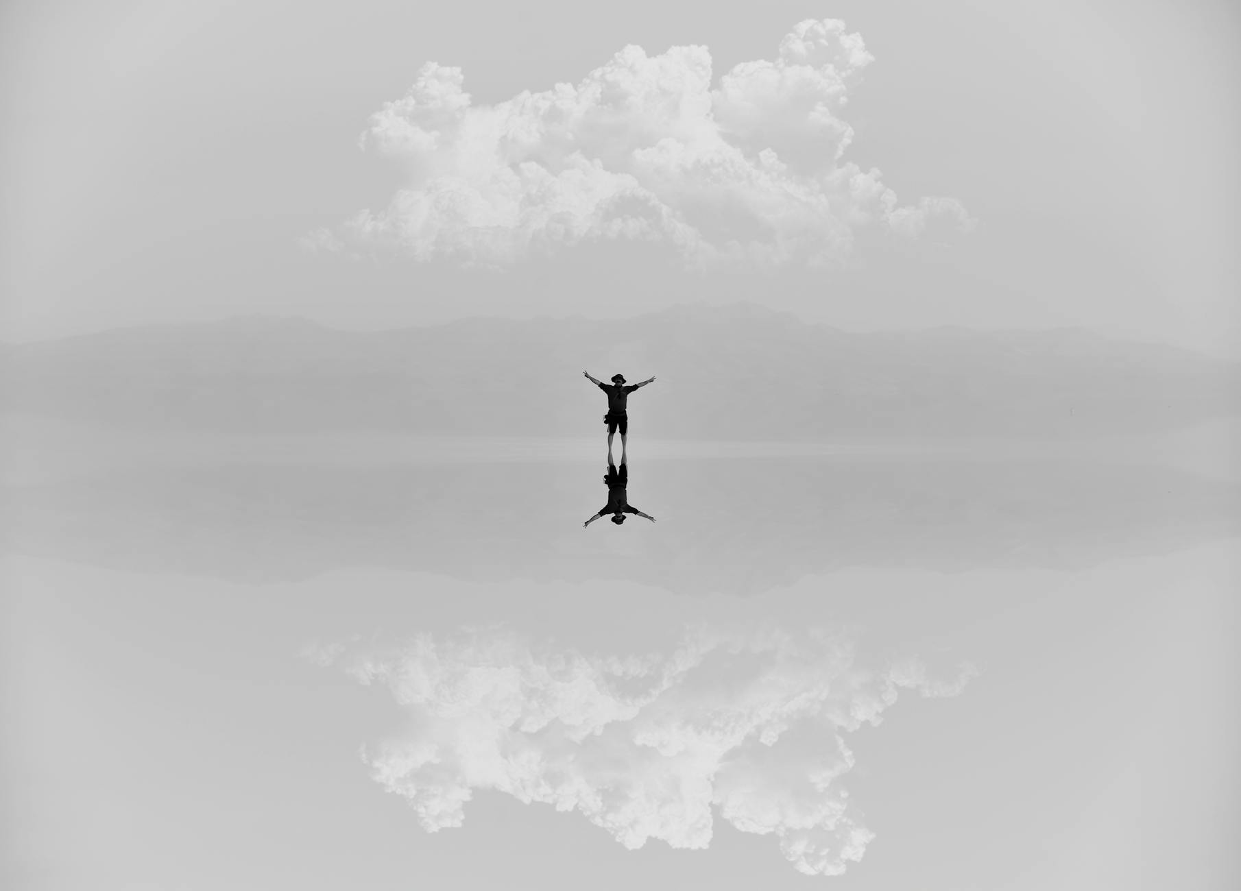 A serene scene of a person with arms raised, reflected in water under cloudy skies.