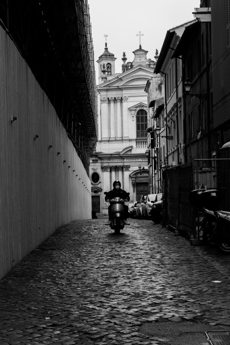 Unrecognizable Motorcyclist Driving Motorbike On Pavement Against Old Urban Church