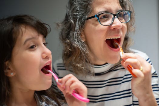 A mother and her daughter brushing their teeth indoors, promoting family hygiene routines.