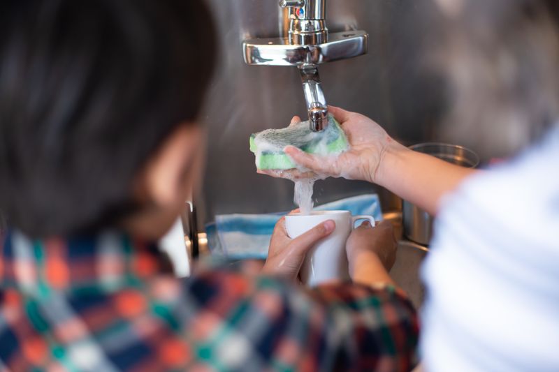 Close-up of hands washing a ceramic mug over the sink with a sponge, showcasing daily routine chores.