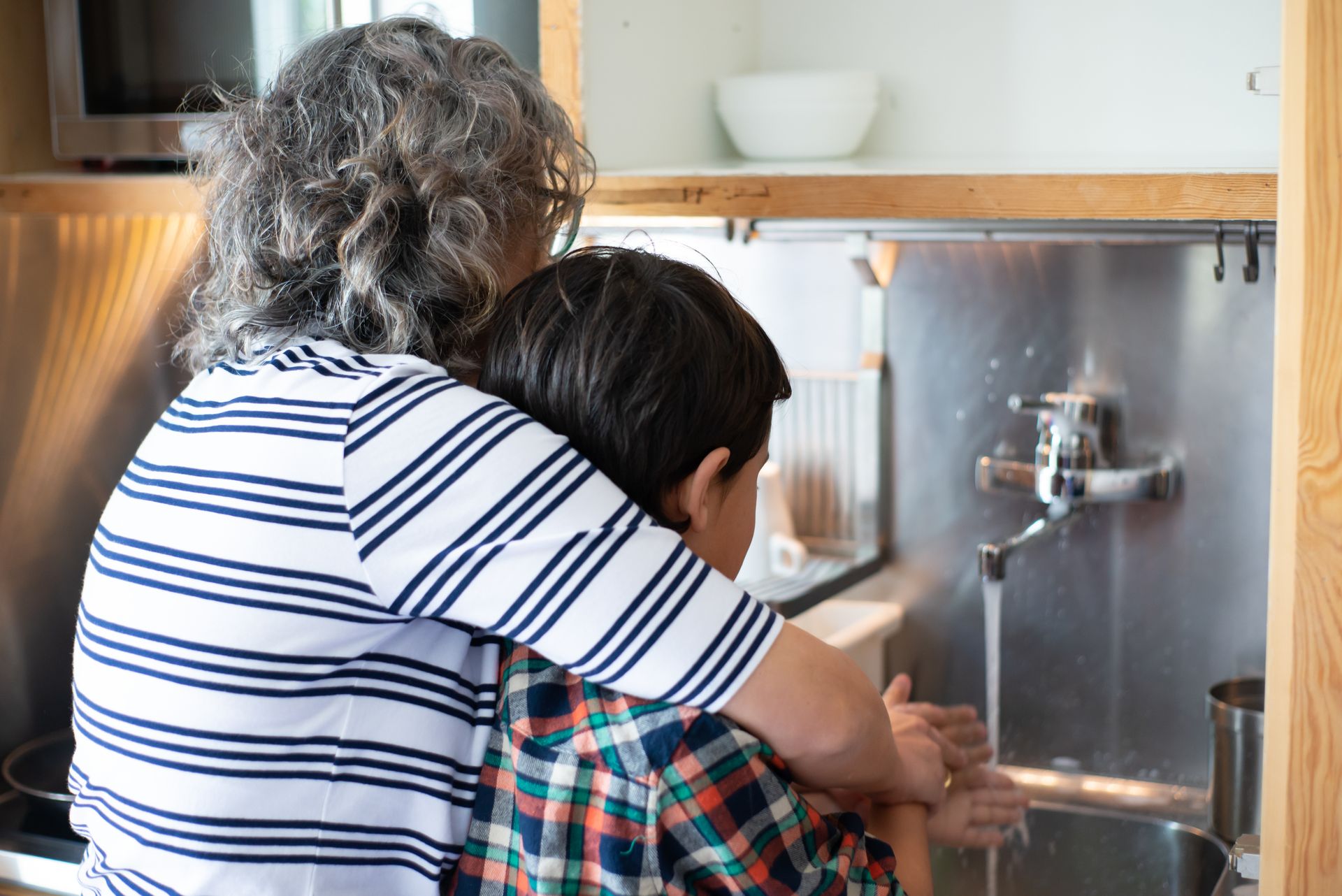 Mother helps her son wash hands at kitchen sink, emphasizing hygiene and family bonding.