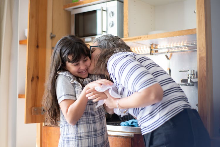 A Mother Kissing Her Daughter On The Cheeks