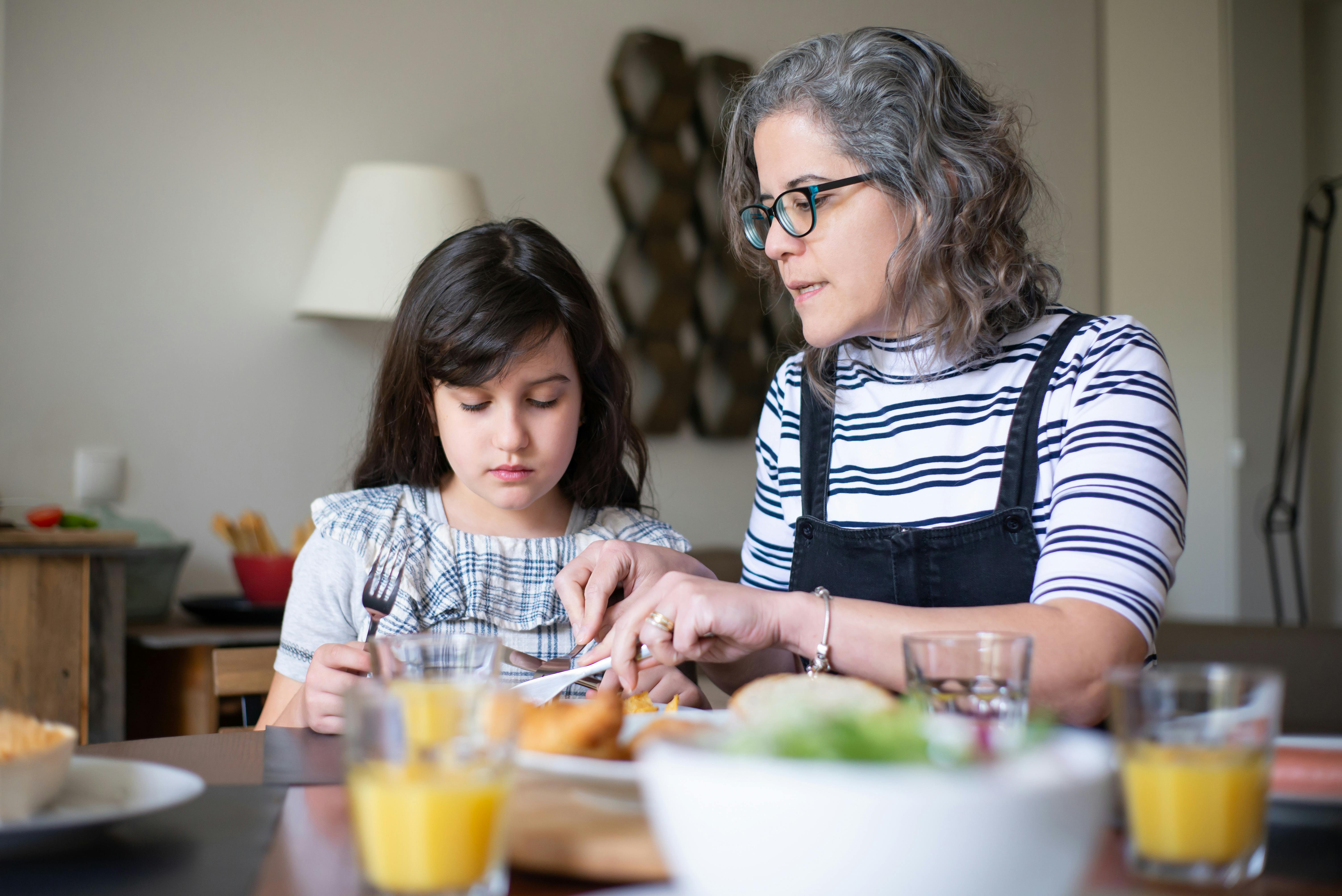 a woman teaching a young girl while cutting food on the plate