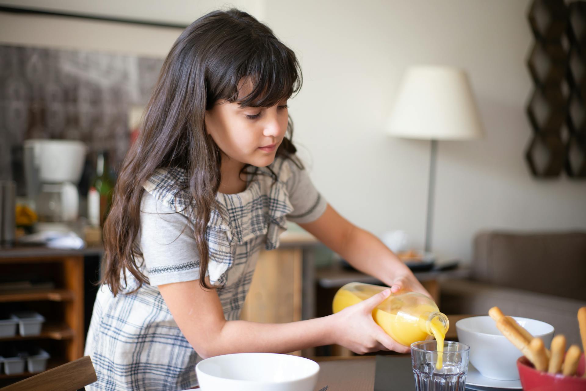 A young girl pours orange juice into a glass during breakfast at home, creating a warm and cozy morning scene.
