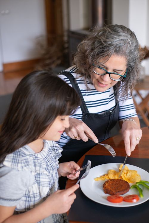 Free A mother teaches her daughter table manners while enjoying a meal together at home. Stock Photo