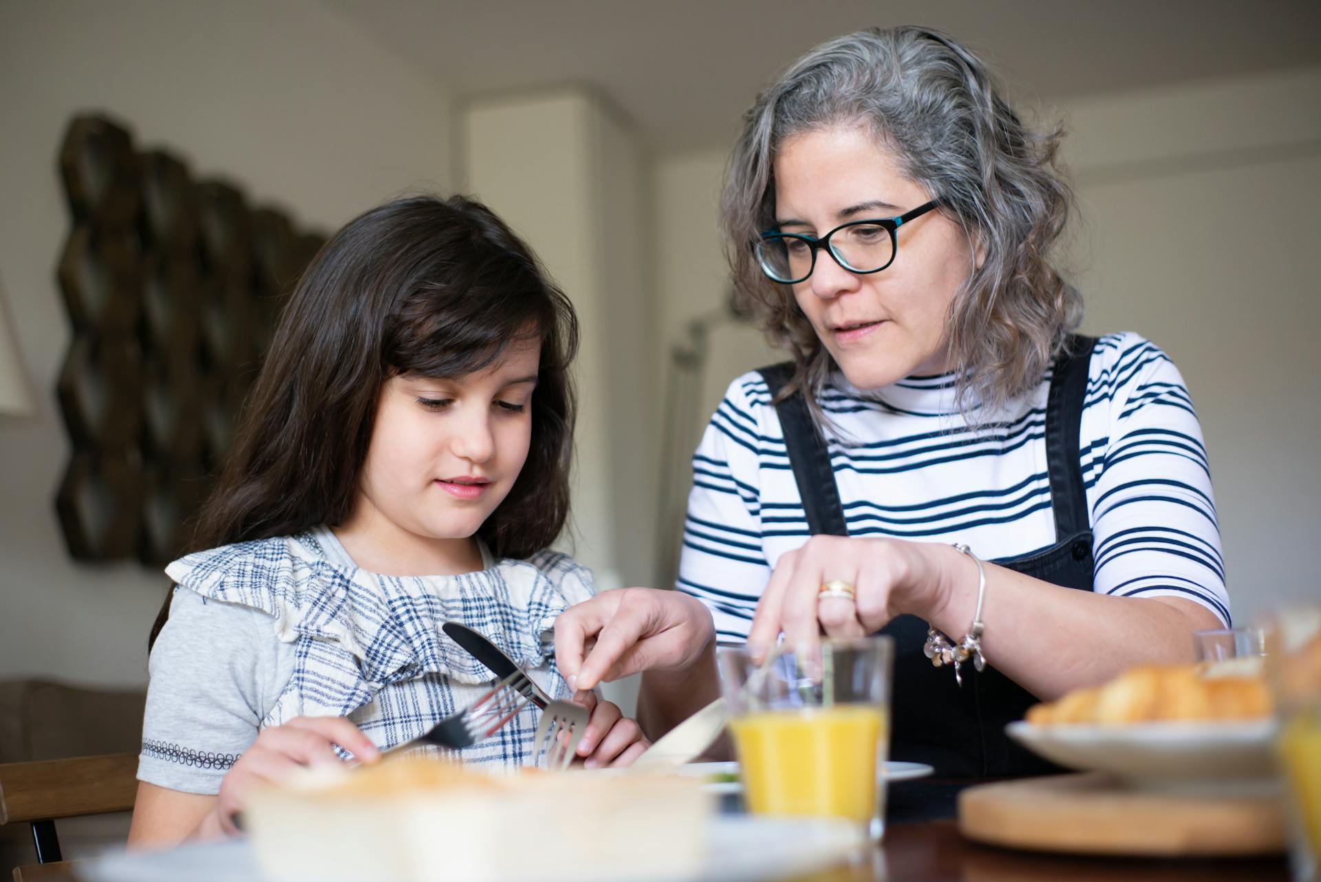 Elderly Woman teaching her Granddaughter Table Manners