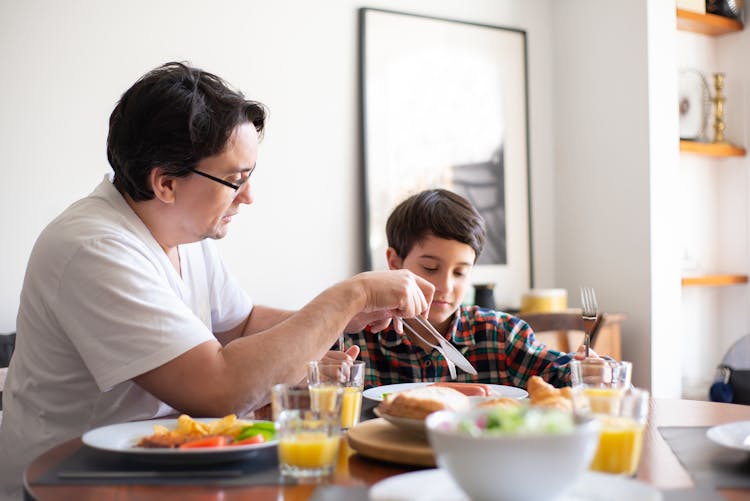 A Man And A Young Boy Eating On Dining Table