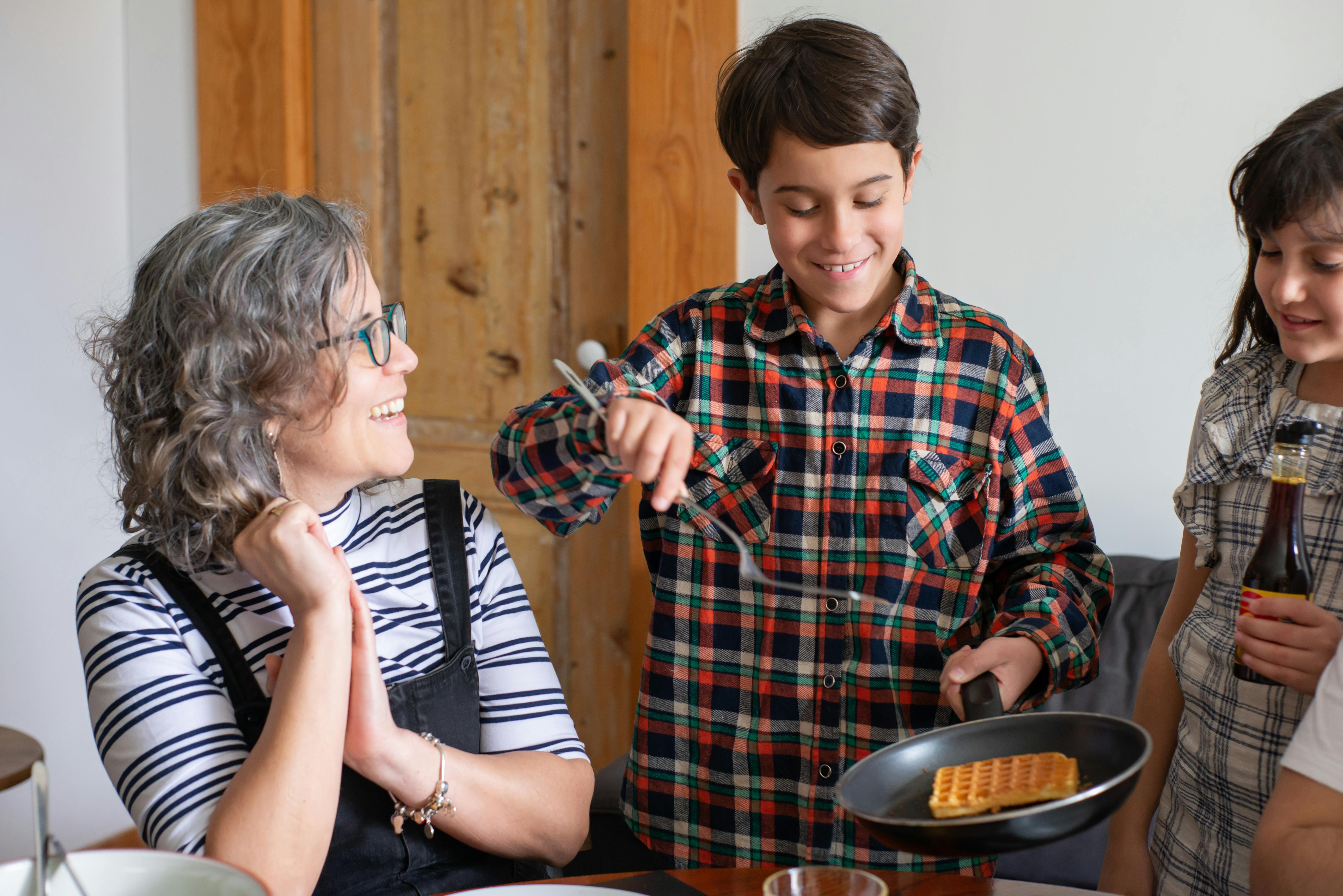 a young boy in plaid long sleeves holding a cooking pan with waffle