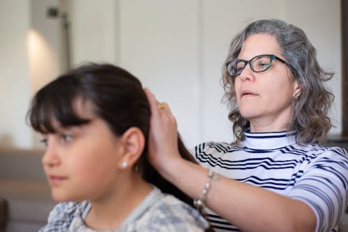 Photo of a Woman with Eyeglasses Fixing the Hair of Her Daughter